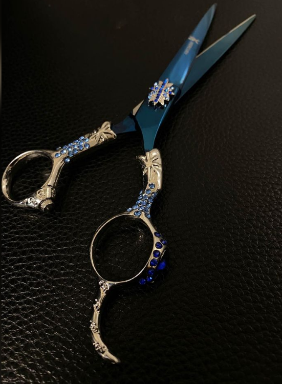 Blue stainless steel hair cutting scissors with ornate silver handles and blue rhinestone accents for professional styling.